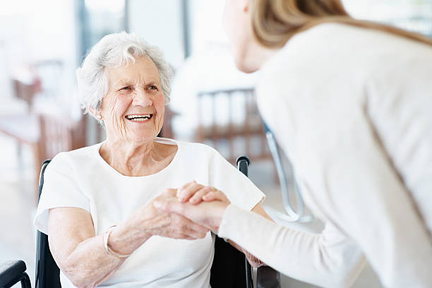 Ladies in wheel chair holding hands with care worker